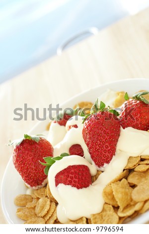 Fresh red strawberries and thick dairy cream on breakfast cereal in a white bowl on a kitchen table