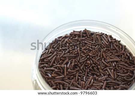 A bed of brown chocolate sprinkles used for cake decoration and dessert toppings in a glass container.