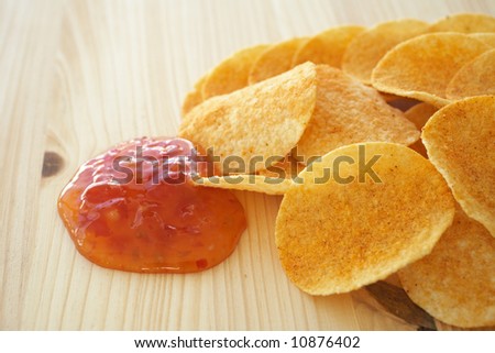 Crispy golden brown potato chips with a hot salsa dip sauce on a wooden presentation plate (shallow depth of field)