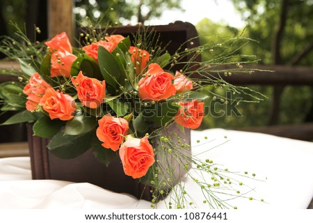 A flower arrangement with red roses and green leaves inside a small wooden treasure chest on a table at a wedding reception