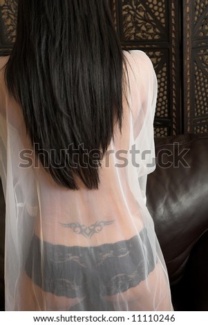 Sexy adult woman in white babydoll and black lacy lingerie. Tattoo on the back shows through the material.