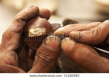 Goldsmith working on an unfinished 22 carat gold ring with his hard working hands. Half of the Diamonds already embedded.