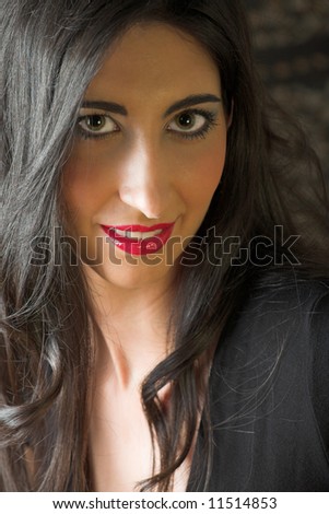 Beautiful young sexy adult Italian woman with long black hair, in formal black dress on a textured wooden background, sitting on a luxurious couch Ð Hard light, high key