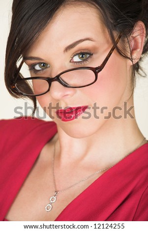Young adult brunette businesswoman with horn rimmed glasses and a red dress. She is Caucasian and wears bright red lipstick.