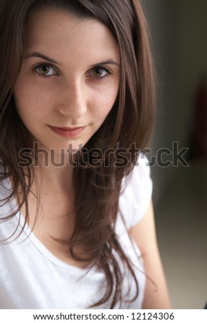 Portrait of a beautiful young adult (teenager) Caucasian woman with light skin and dark brown hair, brown eyes and pink lips, sitting against a wall