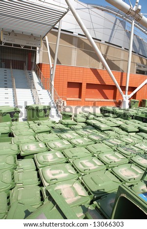 Stacks of green rubbish bins standing outside a sports stadium.