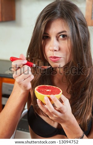 Sexy young adult brunette woman in black lingerie eating a grapefruit for breakfast in her kitchen