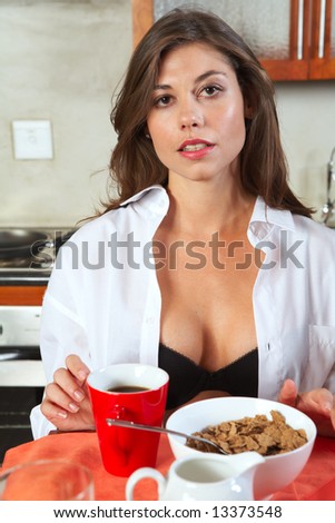 Sexy young adult brunette woman in black lingerie eating breakfast and drinking coffee in her kitchen