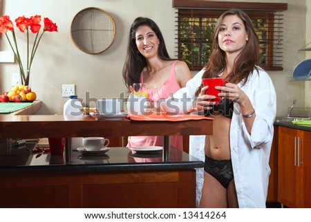 Sexy young adult brunette roommates in lingerie eating breakfast and drinking coffee in their kitchen before work