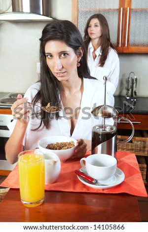 Sexy young adult brunette roommates in lingerie eating breakfast and drinking coffee in their kitchen before work