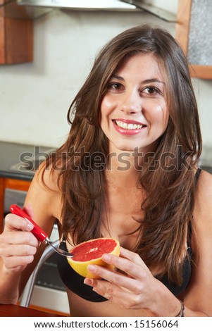 Sexy young adult brunette woman in black lingerie eating a grapefruit for breakfast in her kitchen