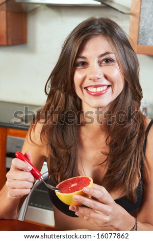 Sexy young adult brunette woman in black lingerie eating a grapefruit for breakfast in her kitchen