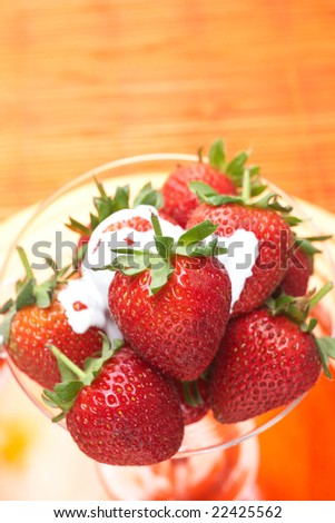 Fresh red strawberries and cream in a martini glass against a brown table background
