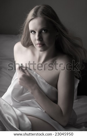 Sensual naked young blonde adult Caucasian woman, wrapped in a satin, silk sheet. High contrast image.