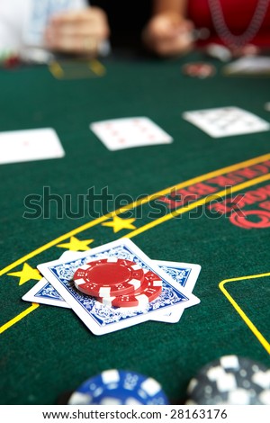 Playing cards, chips and players gambling around a green felt poker table. Shallow Depth of field, focus on the chips and folded hand.