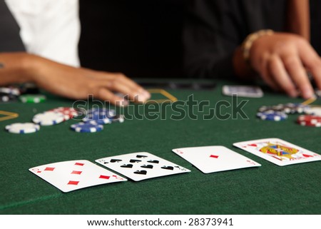 Playing cards, chips and players gambling around a green felt poker table. Shallow Depth of field