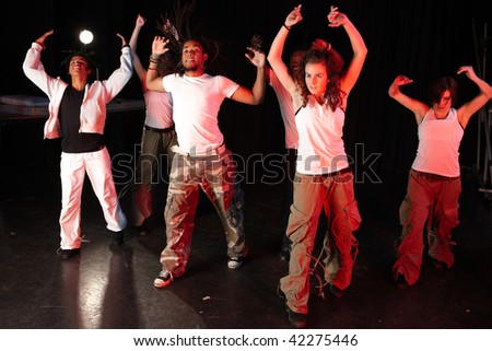 A group of six female and male freestyle hip-hop dancers during dance training session on stage. Lit with spotlights