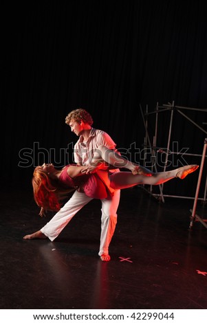 Caucasian male dancer lifting his female partner in a dancing training session on the stage with black background. Lit with spotlights