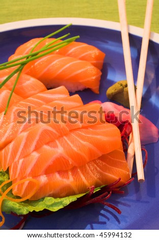 Fresh strips of Norwegian salmon Sashimi and rice Nigiri on a blue plate with a bamboo mat in the background and wooden chopsticks on the plate