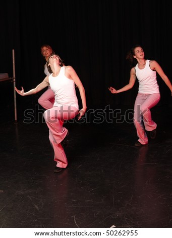 A group of three Caucasian female freestyle hip-hop dancers in a dancing training session. Lit with spotlights