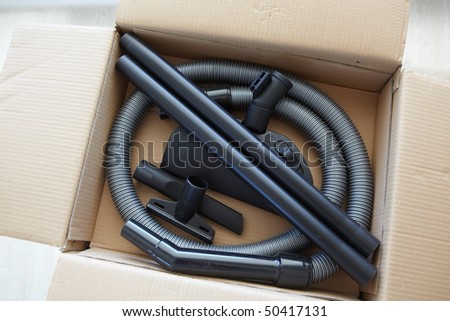 Spare parts and pipes of a new vacuum cleaner in a brown cardboard box, being unpacked