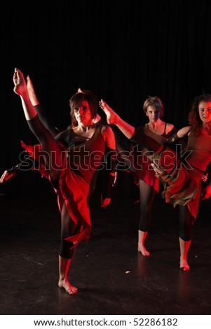 A group of female freestyle hip-hop dancers in a dancing training session. Lit with spotlights. Movement on edges of dancers, kicking high.