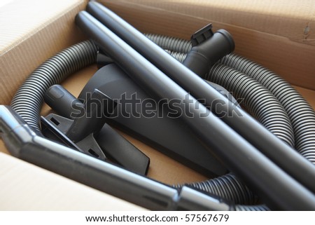 Spare parts and pipes of a new vacuum cleaner in a brown cardboard box, being unpacked
