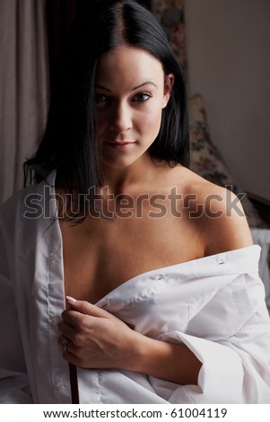 Young brunette caucasian woman wearing a white man\'s shirt sitting in her bedroom