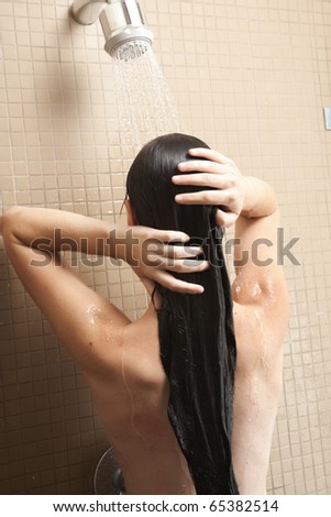 Sexy young adult Caucasian woman with long auburn hair and petite breasts taking a shower in a tile and glass modern bathroom.