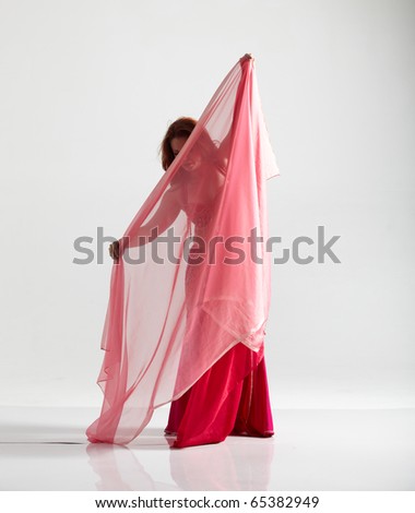 Lithe adult caucasian belly dancer with red hair and pink belly dancing outfit performing a dance with veils on a white background. Not Isolated
