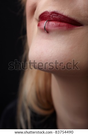 Pierced red lips of young adult caucasian female woman against a dark background.