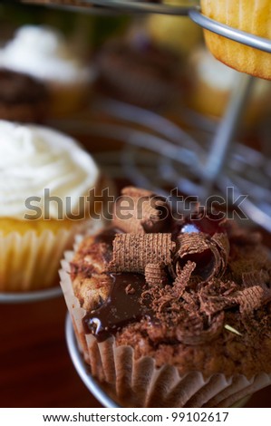 Chocolate and cream filled cupcakes with glazed cherries and chocolate shavings on a display stand. Shallow Depth of field with focus on the chocolate cupcake