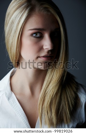 Young adult caucasian woman with long blonde hair and green eyes wearing a plain white shirt with flawless skin and natural makeup.