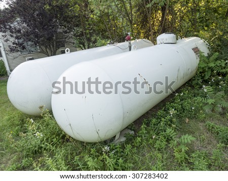 Two scratched propane gas tanks near house in the rural area. Source for cooking and heating.