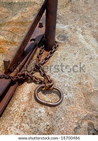 Rusty chain with shackle around a steel pole on a granite stone ground