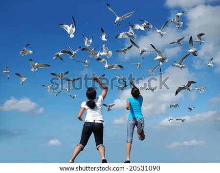 Girls feeding a flock of birds (seagulls) flying in the air