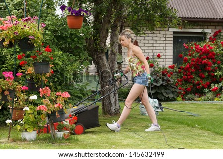 Woman mows the garden with electric mower