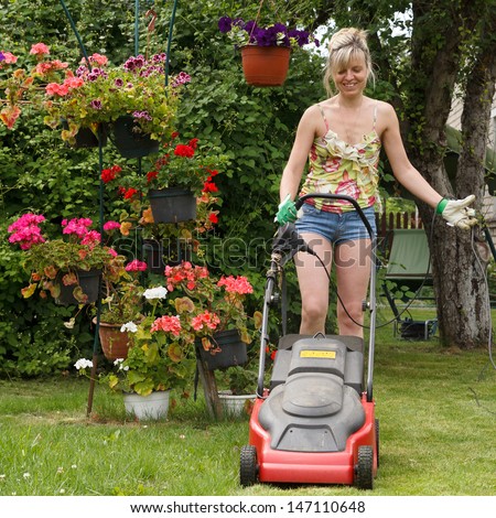 Woman mows the lawn with an electric lawn mower