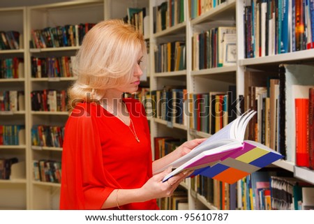 A pretty young adult woman enjoys her book while researching in a library.