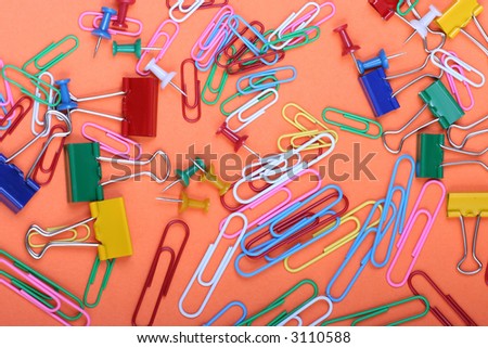 Office stationary - paperclips clamps and tacks strewn over orange background