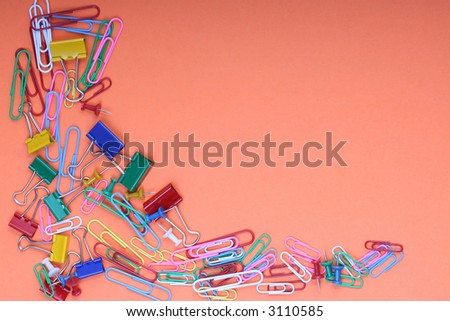 Office stationary (Paperclips, clamps and tacks) strewn over background bottom left corner orange background