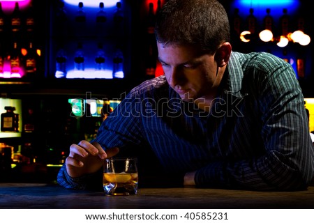 Worried man sitting at bar with whiskey glass. Dark night scene. Colored background