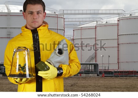 Man with gasmask and plant standing at oil reservoirs