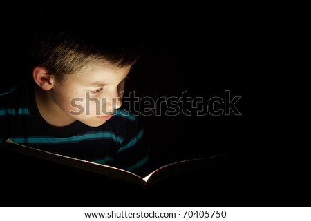 Boy reading bedtime story, dark photo, key light coming from book