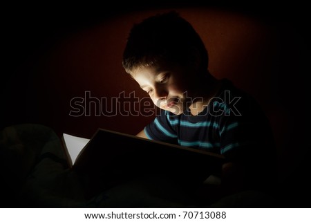 Boy reading bedtime story, dark photo, key light coming from book