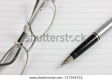 A fountain pen and glasses on a lined notepad with copy space. Logos removed