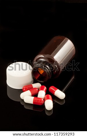 Red and white capsules spilling from a bottle. With reflection.