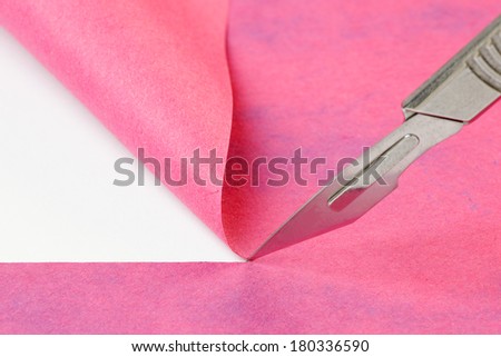 Close up of a scalpel cutting a line through a sheet of colored art paper, with a fold in the background