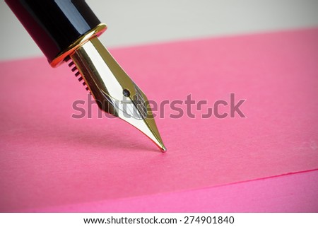 Close up of a gold fountain pen nib on a pink note pad, with vignette