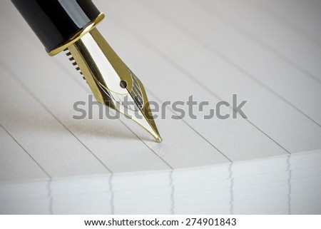 Close up of a gold fountain pen nib on a note pad, with vignette